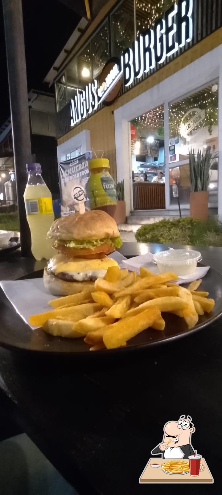 Burger con papas en terraza nocturna con el letrero ANGUS BURGER iluminado al fondo